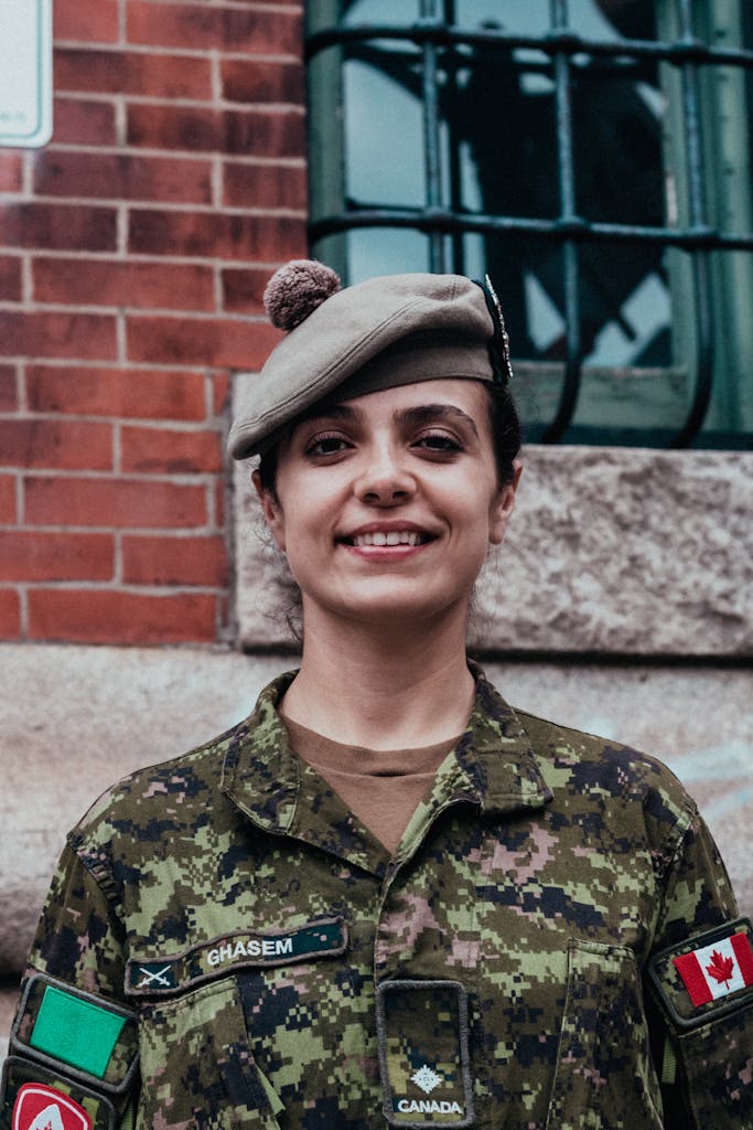 Portrait of a smiling soldier in a Canadian military uniform standing against a brick wall outdoors.