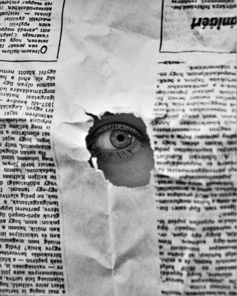 A mysterious eye peering through a hole in a black and white newspaper, creating an intriguing visual.